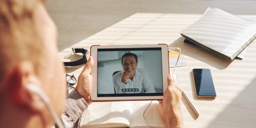 Businessman video conferencing with leader on digital tablet at desk in office