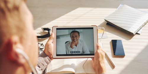 Businessman video conferencing with leader on digital tablet at desk in office
